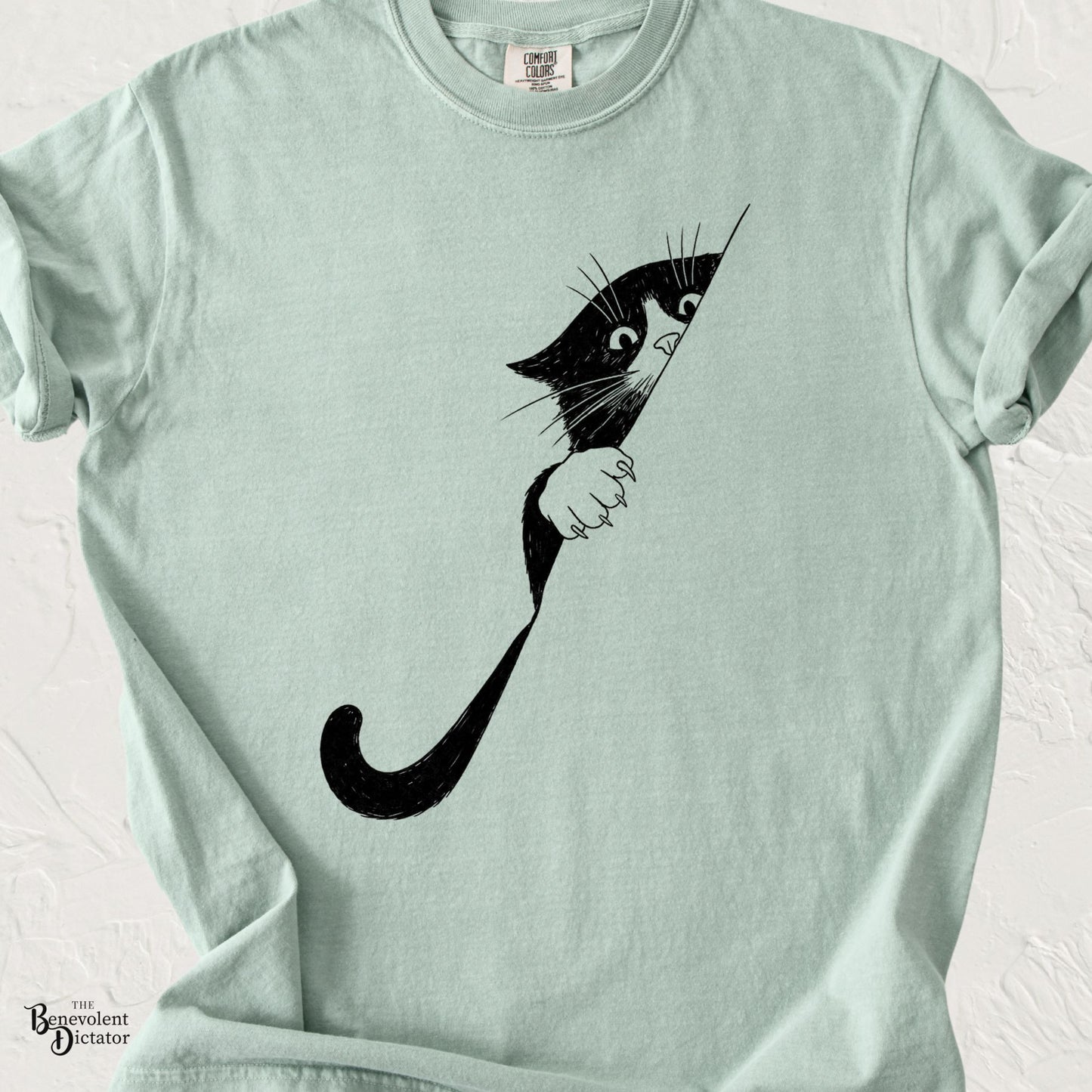 Minimalist black and white cat peeking around a corner with wide eyes and a curled tail on a Comfort Colors T-shirt.