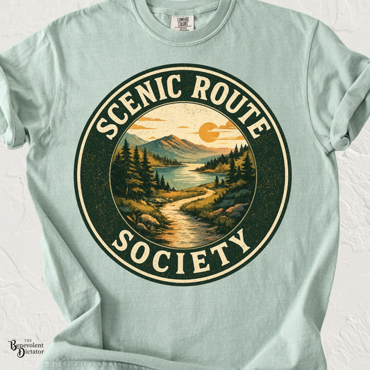 Vintage-style circular landscape featuring a winding trail, mountains, lake, and the words "Scenic Route Society" in distressed retro typography on a transparent background.