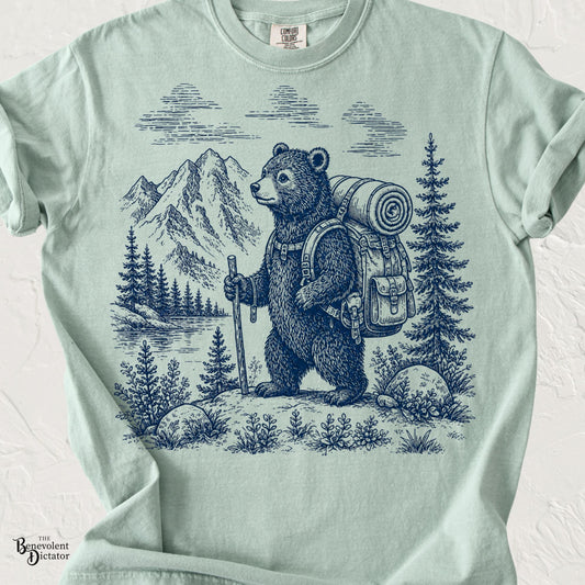 Vintage blue line-art illustration of a backpacking bear standing beside a mountain lake with pine trees on a Comfort Colors shirt.