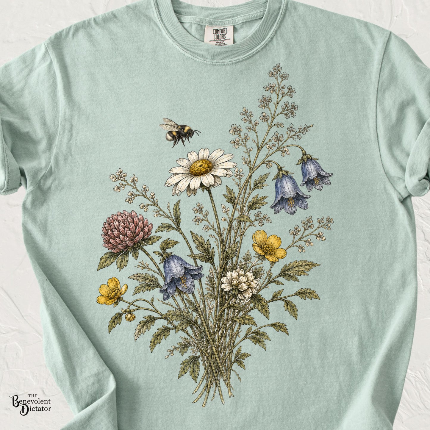 Vintage wildflower bouquet t-shirt featuring daisies, clover, blue bell-shaped flowers, yellow wildflowers, delicate foliage, and a hovering bumblebee.