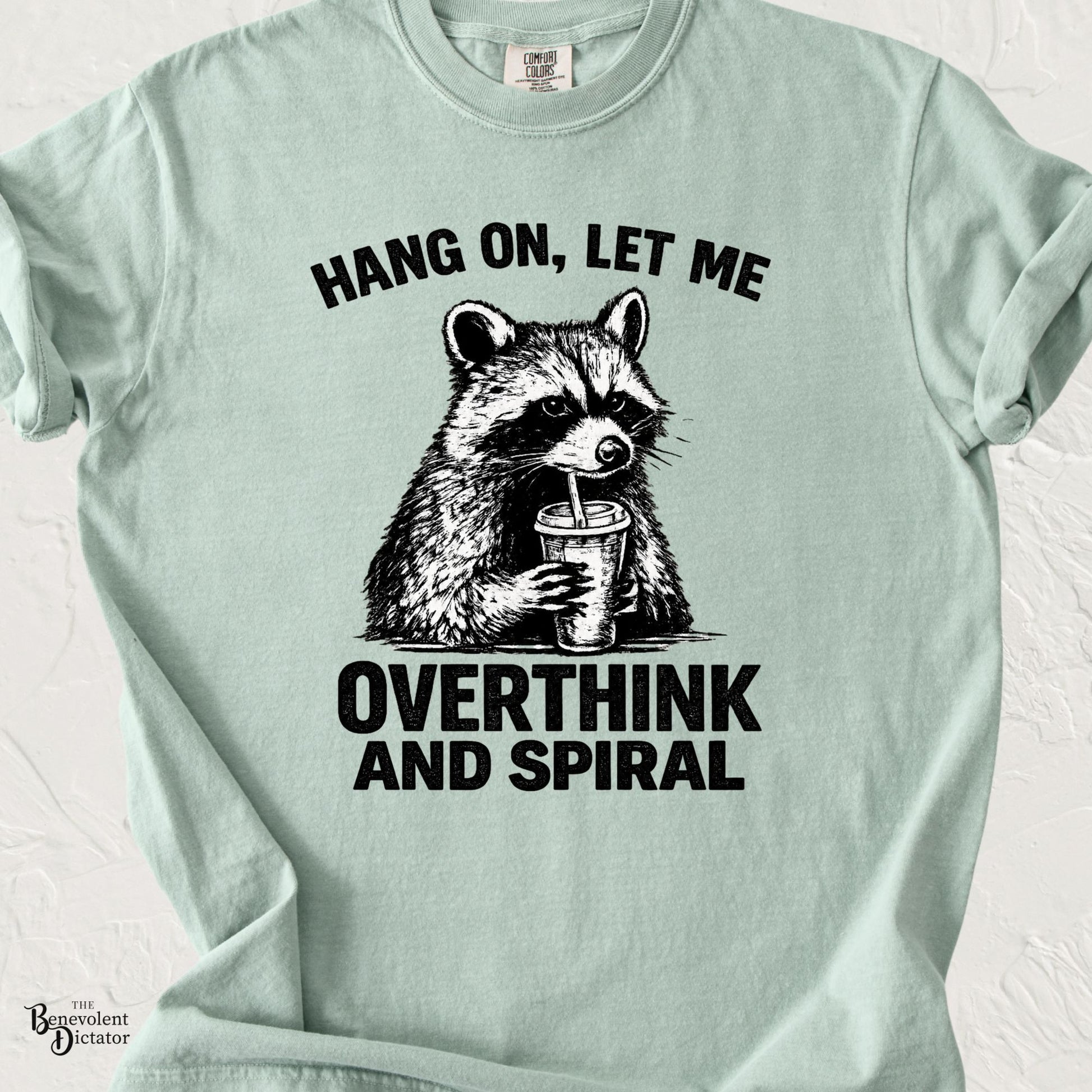 Bay Comfort Colors t-shirt featuring a vintage raccoon drinking from a cup with bold black text reading “Hang On, Let Me Overthink and Spiral.”
