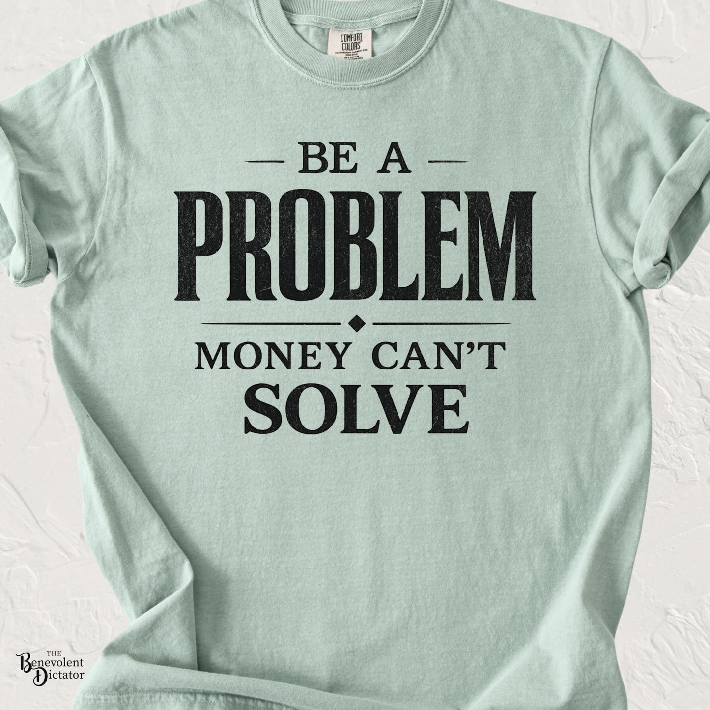 Mint green graphic t-shirt with bold typography reading “Be a Problem Money Can’t Solve” in distressed black lettering.
