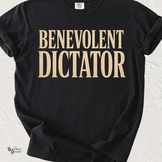 graphic t-shirt featuring bold vintage serif typography reading Benevolent Dictator in distressed cream lettering.