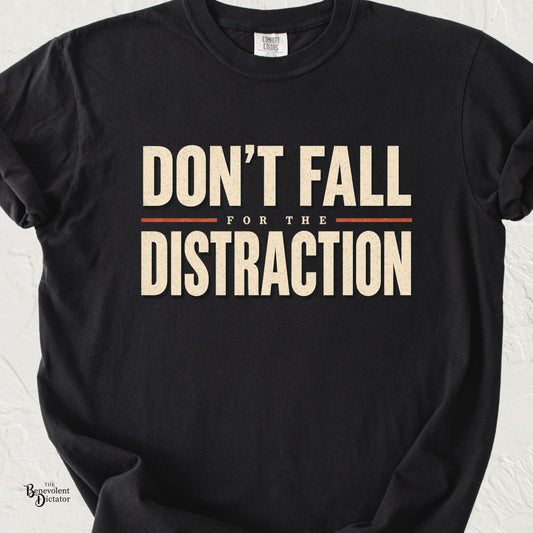 Black graphic t-shirt with distressed cream and rust typography reading “Don’t Fall for the Distraction,” a bold message about questioning deflection and those in power.