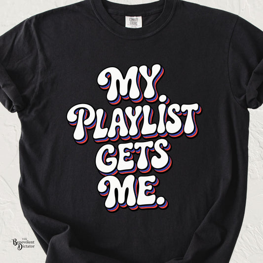 Black Comfort Colors t-shirt with bold retro 1970s-style typography reading “My Playlist Gets Me” in white with red and blue dimensional accents.