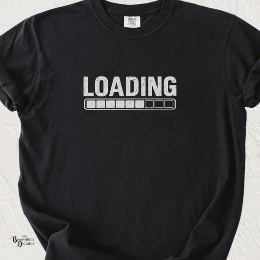Black Comfort Colors t-shirt with distressed grey text reading “Loading” above a partially filled progress bar in a minimalist graphic design.