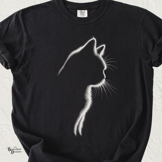 Black Comfort Colors t-shirt featuring a minimalist white illuminated outline of a cat in profile, with delicate glowing fur and whisker details against the dark fabric.