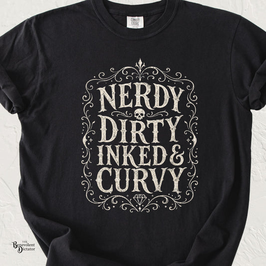 Black Comfort Colors t-shirt with distressed ivory typography reading Nerdy Dirty Inked & Curvy, surrounded by ornate vintage flourishes, a skull, and a diamond.