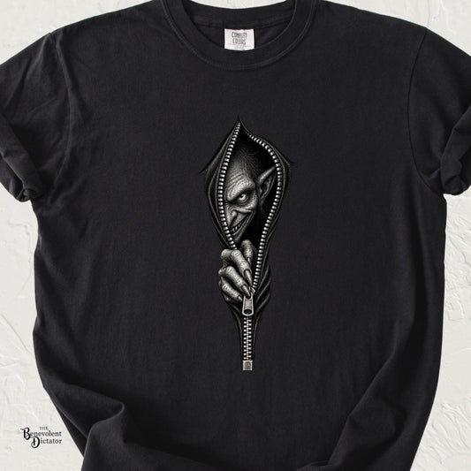 Black Comfort Colors t-shirt featuring a sinister goblin emerging through an open zipper, gripping the zipper pull from inside.