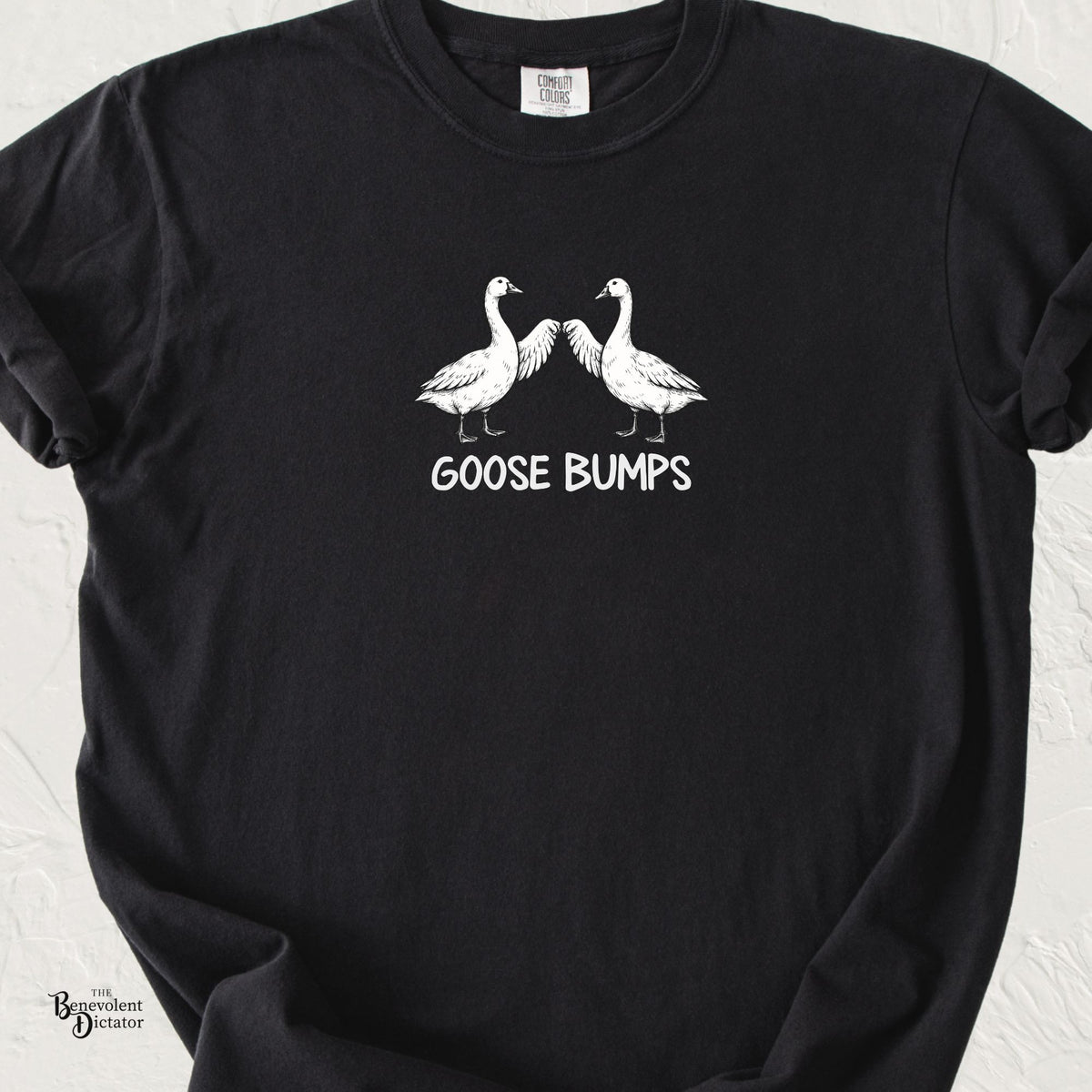 Black Comfort Colors t-shirt featuring two illustrated geese touching wings in a fist-bump pose above the words “Goose Bumps.”