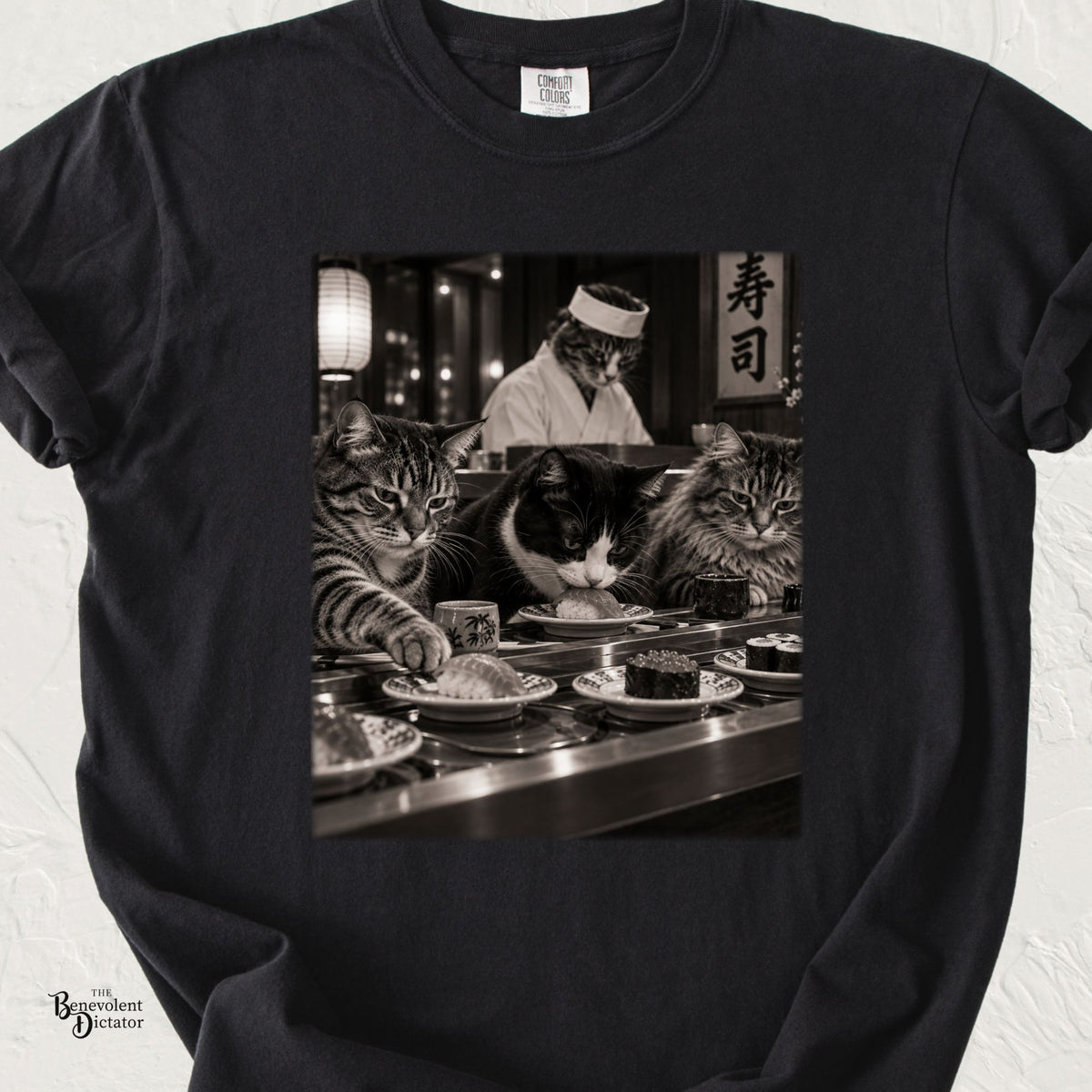 Black Comfort Colors t-shirt featuring a black-and-white scene of three unimpressed cats sitting at a conveyor belt sushi restaurant with a cat sushi chef behind the counter.