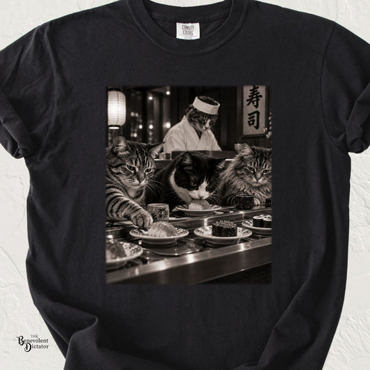 Black Comfort Colors t-shirt featuring a black-and-white scene of three unimpressed cats sitting at a conveyor belt sushi restaurant with a cat sushi chef behind the counter.