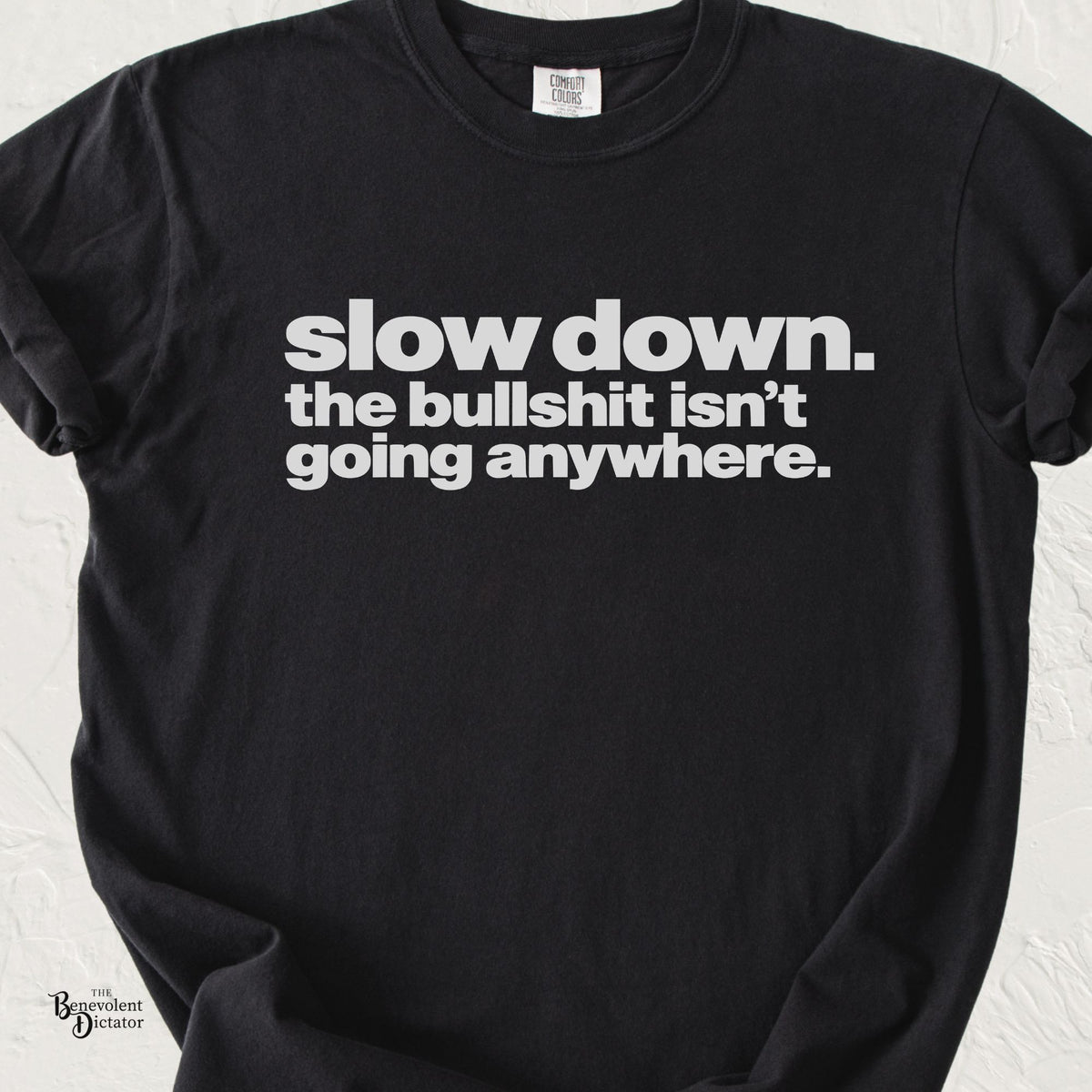 A black short-sleeve t-shirt with bold white text reading 'slow down. the bullshit isn't going anywhere.