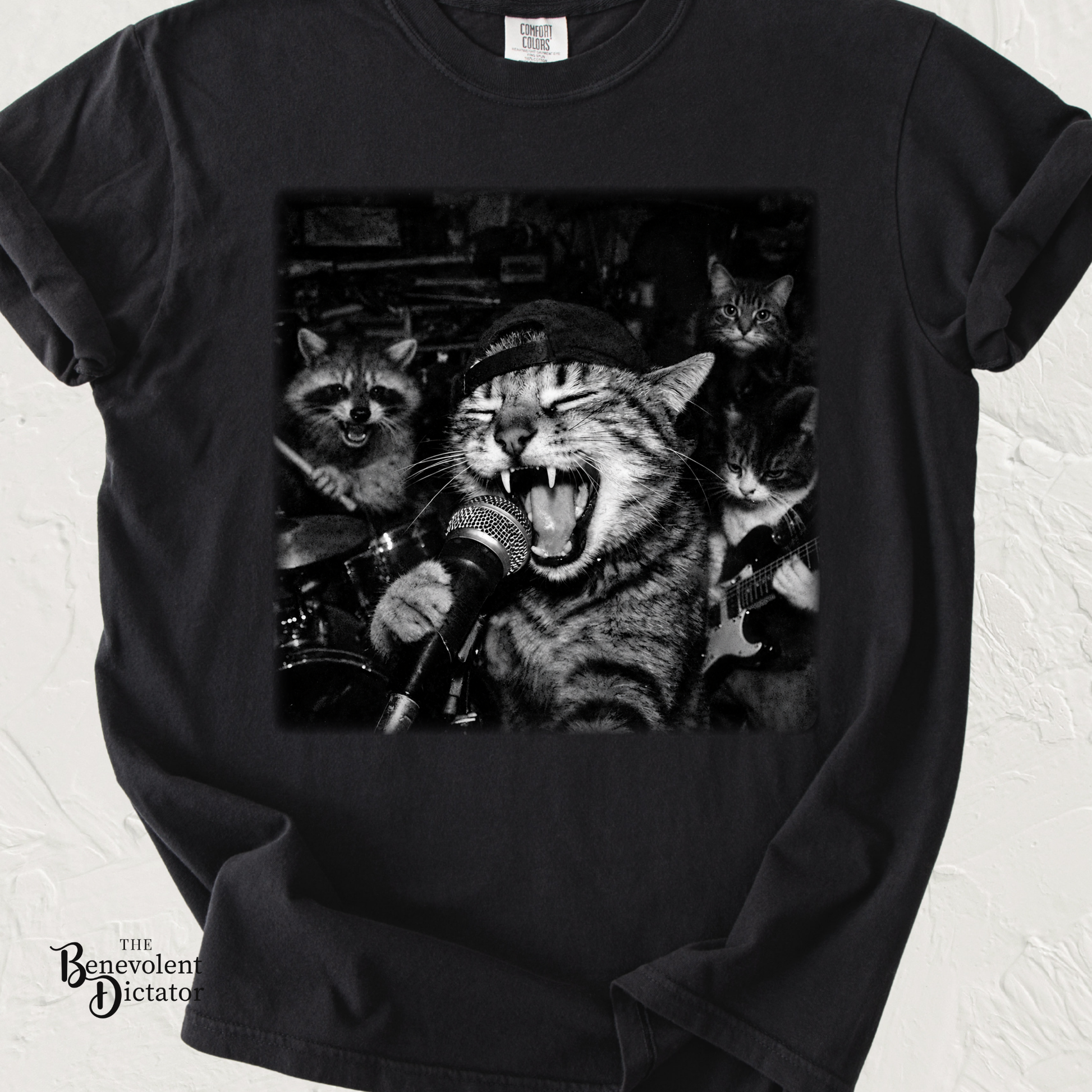 Black graphic t-shirt featuring a chaotic cat garage band in monochrome artwork with a screaming lead singer at a microphone, raccoon drummer, and cat guitarist.