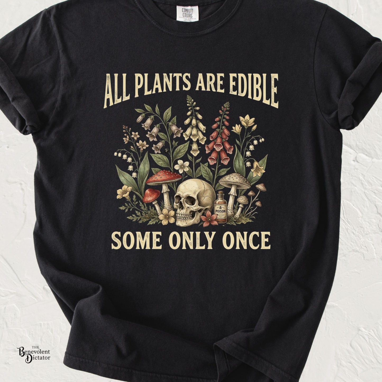 Black Comfort Colors t-shirt featuring vintage botanical artwork with flowers, mushrooms, a skull, and poison bottle alongside the quote “All Plants Are Edible. Some Only Once.”