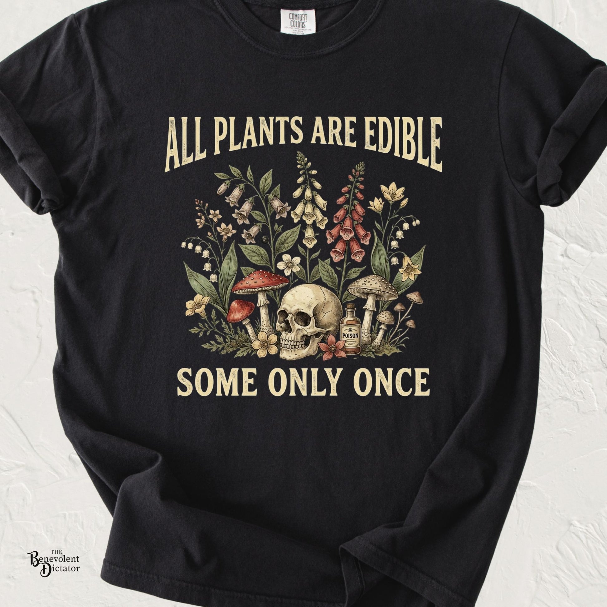 Black Comfort Colors t-shirt featuring vintage botanical artwork with flowers, mushrooms, a skull, and poison bottle alongside the quote “All Plants Are Edible. Some Only Once.”