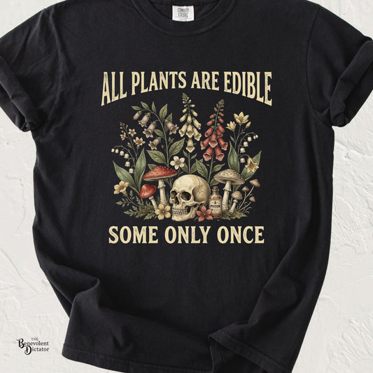 Black Comfort Colors t-shirt featuring vintage botanical artwork with flowers, mushrooms, a skull, and poison bottle alongside the quote “All Plants Are Edible. Some Only Once.”