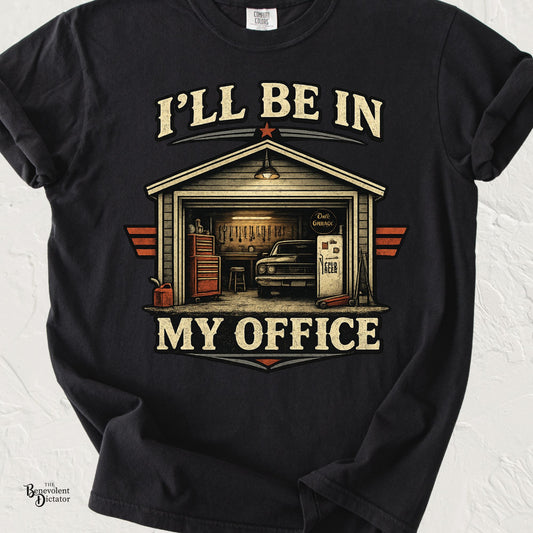 Black Comfort Colors t-shirt featuring a vintage garage illustration with a classic car, tools, toolbox, and fridge, alongside the phrase “I’ll Be In My Office.”