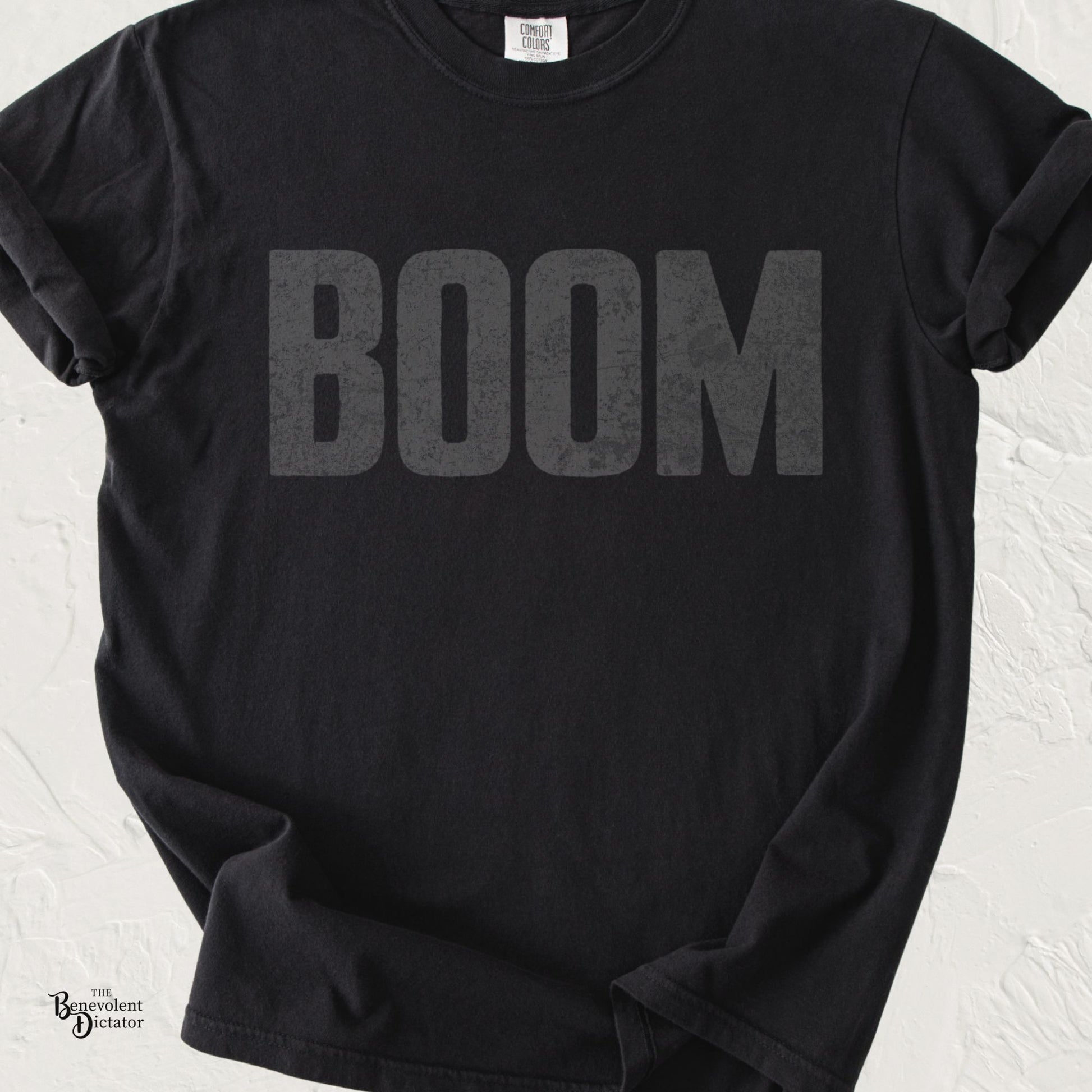 Black Comfort Colors t-shirt featuring the word "BOOM" in oversized distressed charcoal gray typography across the chest.