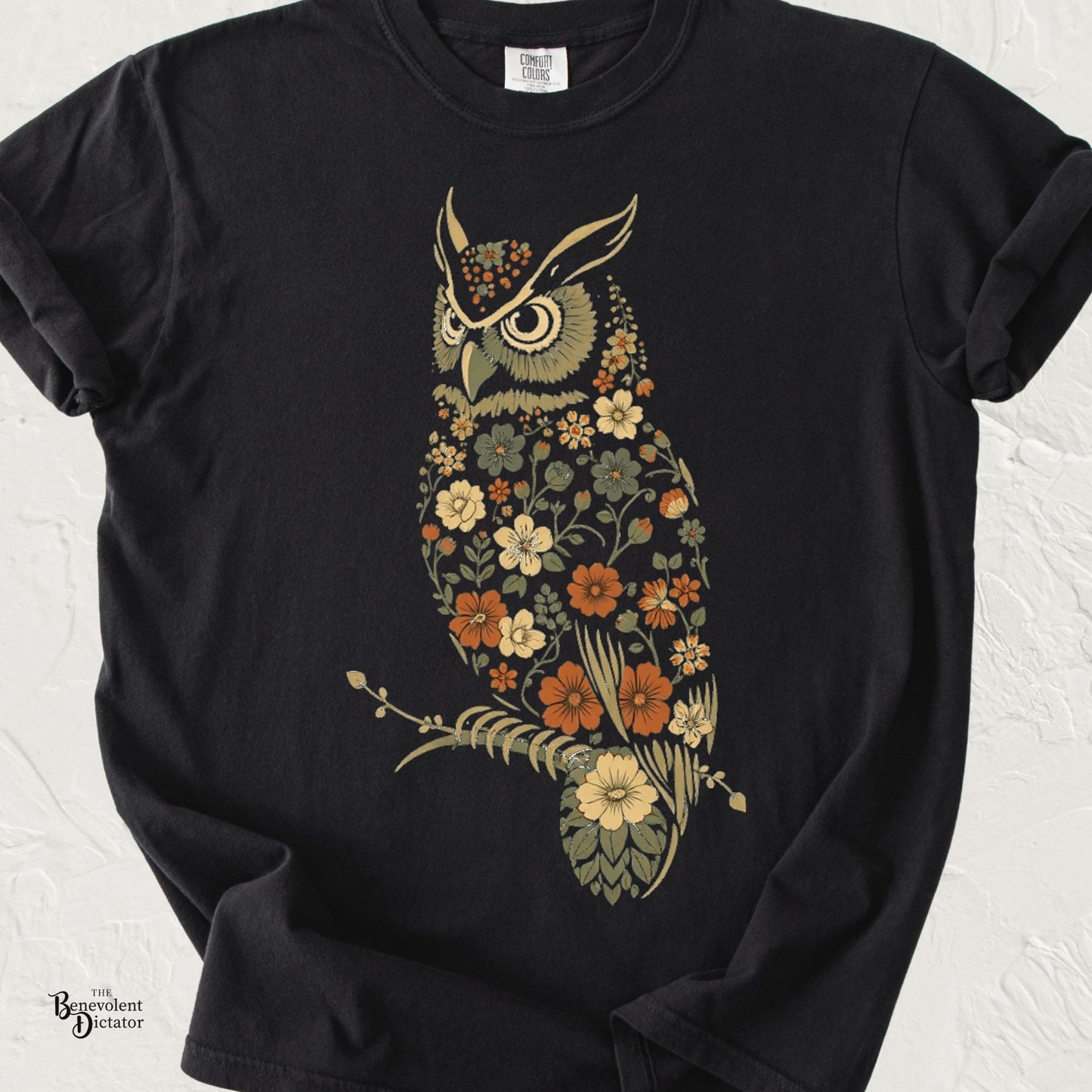 Comfort Colors black t-shirt featuring a stylized owl made entirely of vintage wildflowers in muted earth tones perched on a delicate branch.