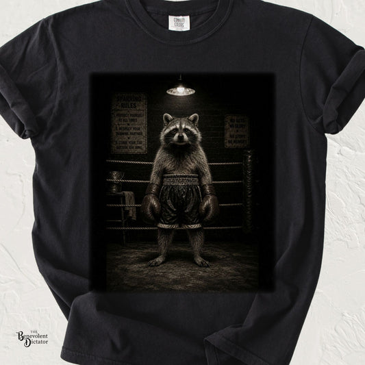 Vintage-style illustration of a determined raccoon wearing oversized boxing gloves and trunks, standing confidently in a dimly lit boxing ring on a black Comfort Colors T-shirt.