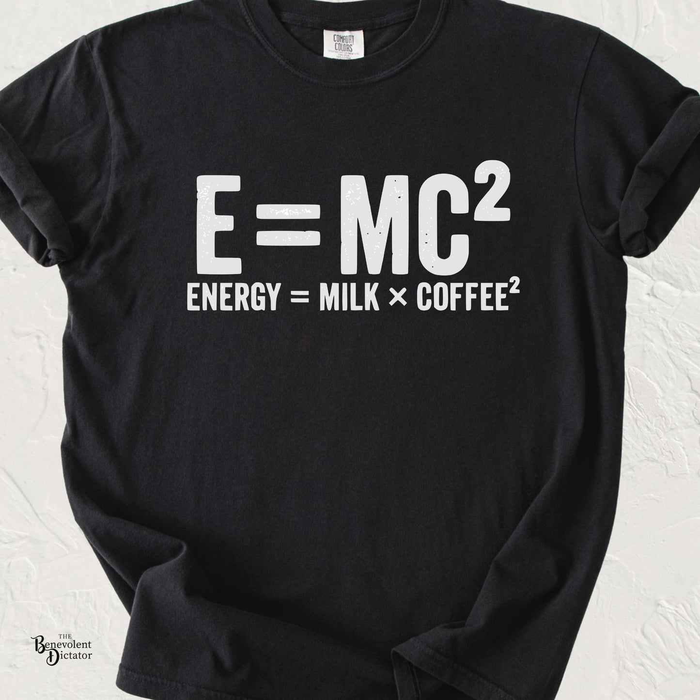 Minimalist typography T-shirt featuring the parody equation "E = MC²" with the caption "Energy = Milk × Coffee²" printed in distressed white lettering on a black Comfort Colors shirt.