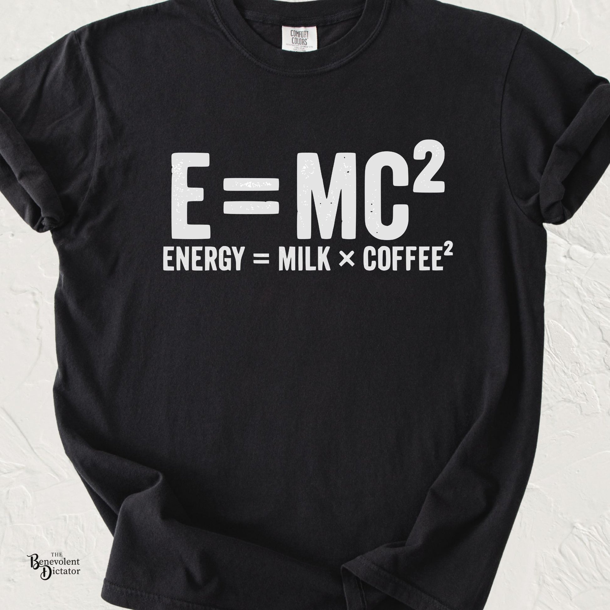 Minimalist typography T-shirt featuring the parody equation "E = MC²" with the caption "Energy = Milk × Coffee²" printed in distressed white lettering on a black Comfort Colors shirt.