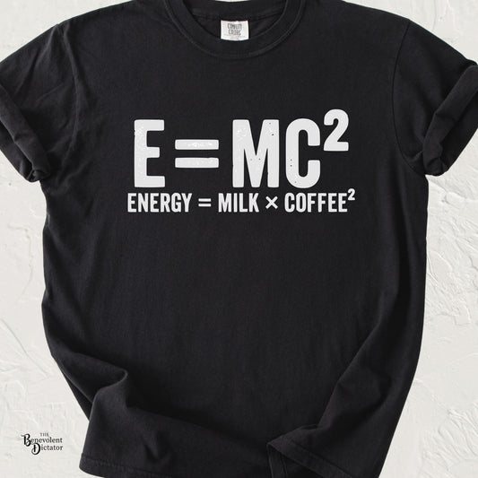 Minimalist typography T-shirt featuring the parody equation "E = MC²" with the caption "Energy = Milk × Coffee²" printed in distressed white lettering on a black Comfort Colors shirt.