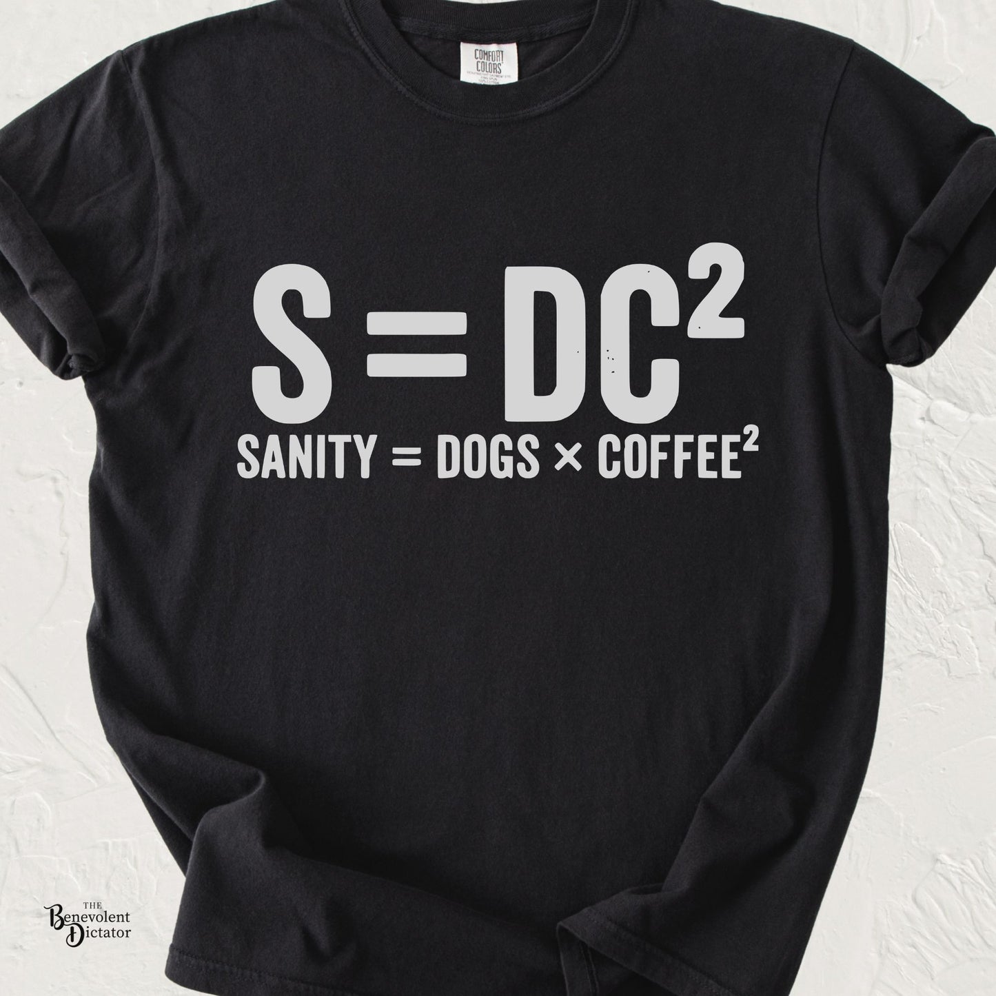Funny typography T-shirt featuring the parody equation "S = DC²" with the caption "Sanity = Dogs × Coffee²" in distressed white lettering on a black Comfort Colors shirt.