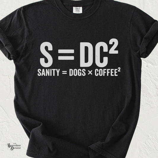 Funny typography T-shirt featuring the parody equation "S = DC²" with the caption "Sanity = Dogs × Coffee²" in distressed white lettering on a black Comfort Colors shirt.