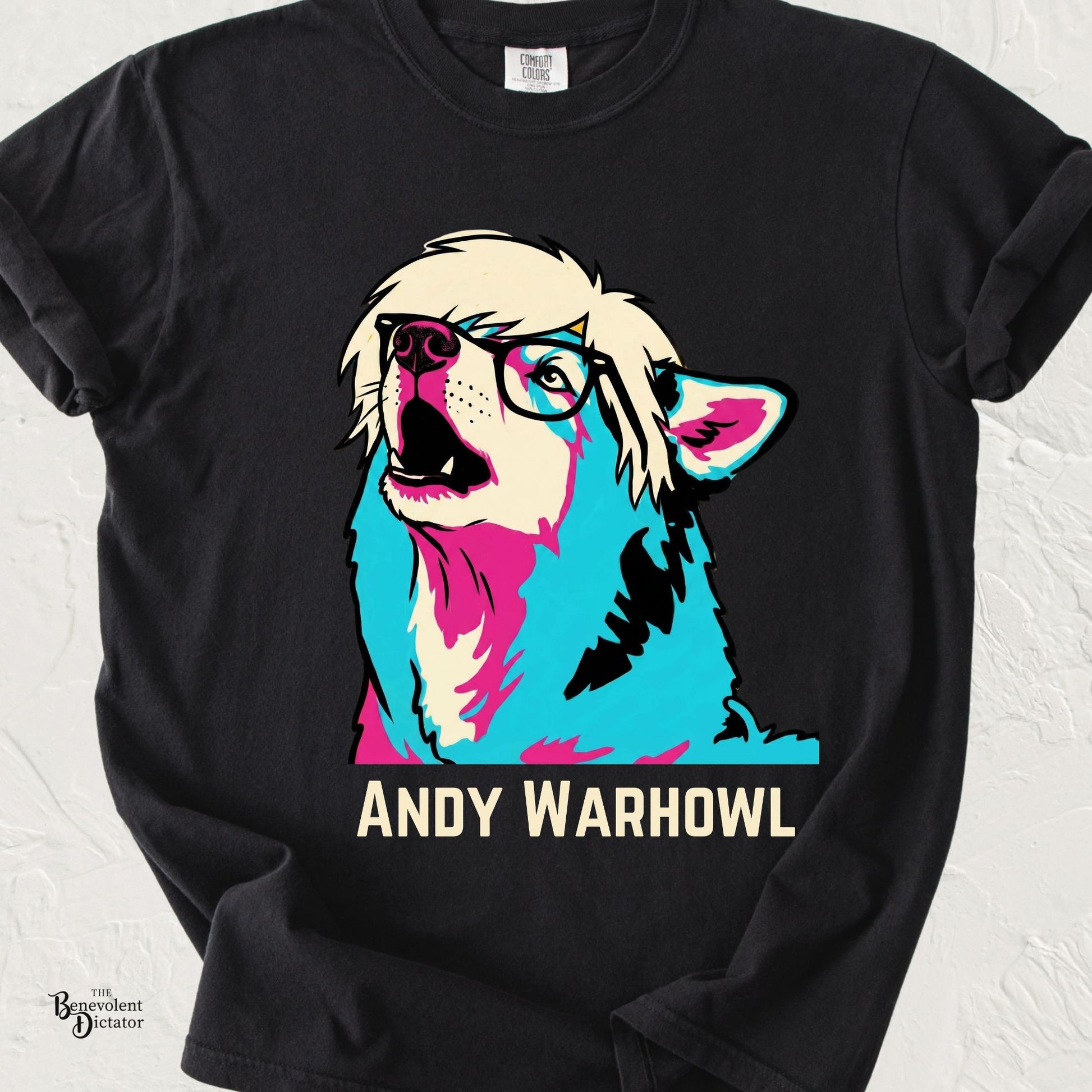 Colorful pop art illustration of a shaggy dog with oversized black glasses and platinum hair howling upward above the text "Andy Warhowl" on a Comfort Colors® t-shirt.