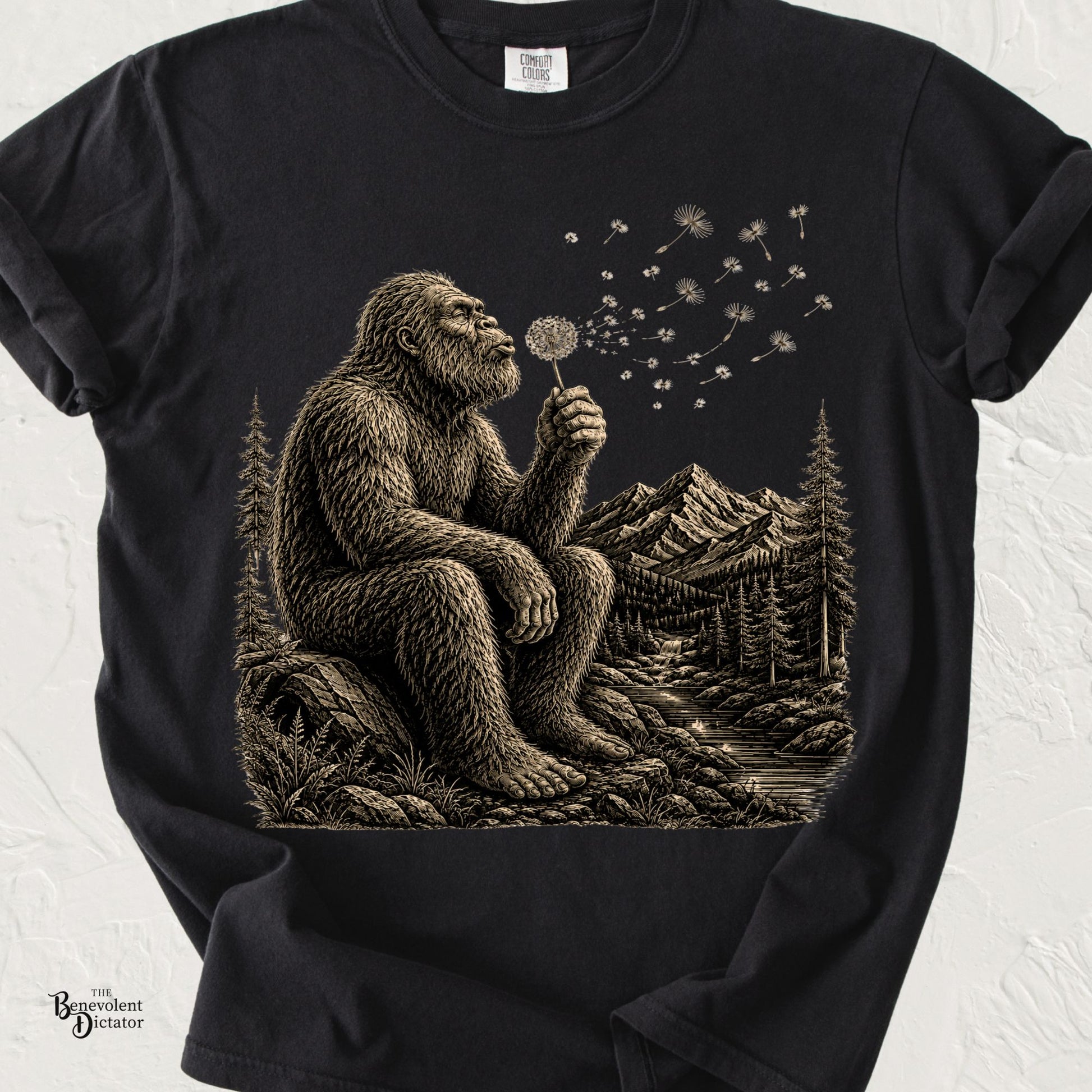 Vintage-style Bigfoot sitting on a rock blowing a dandelion with mountains, forest, and river in the background.