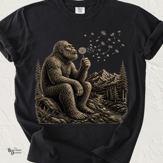 Vintage-style Bigfoot sitting on a rock blowing a dandelion with mountains, forest, and river in the background.