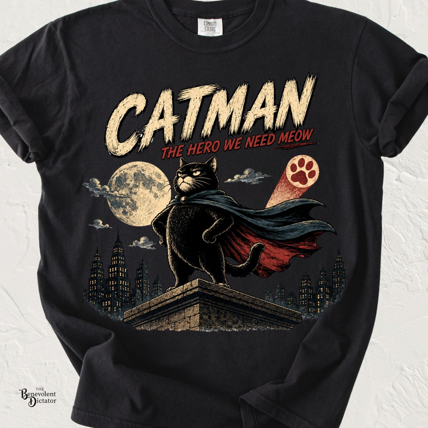 Vintage superhero-style black cat wearing a cape on a rooftop under a full moon with the words "Catman – The Hero We Need Meow."