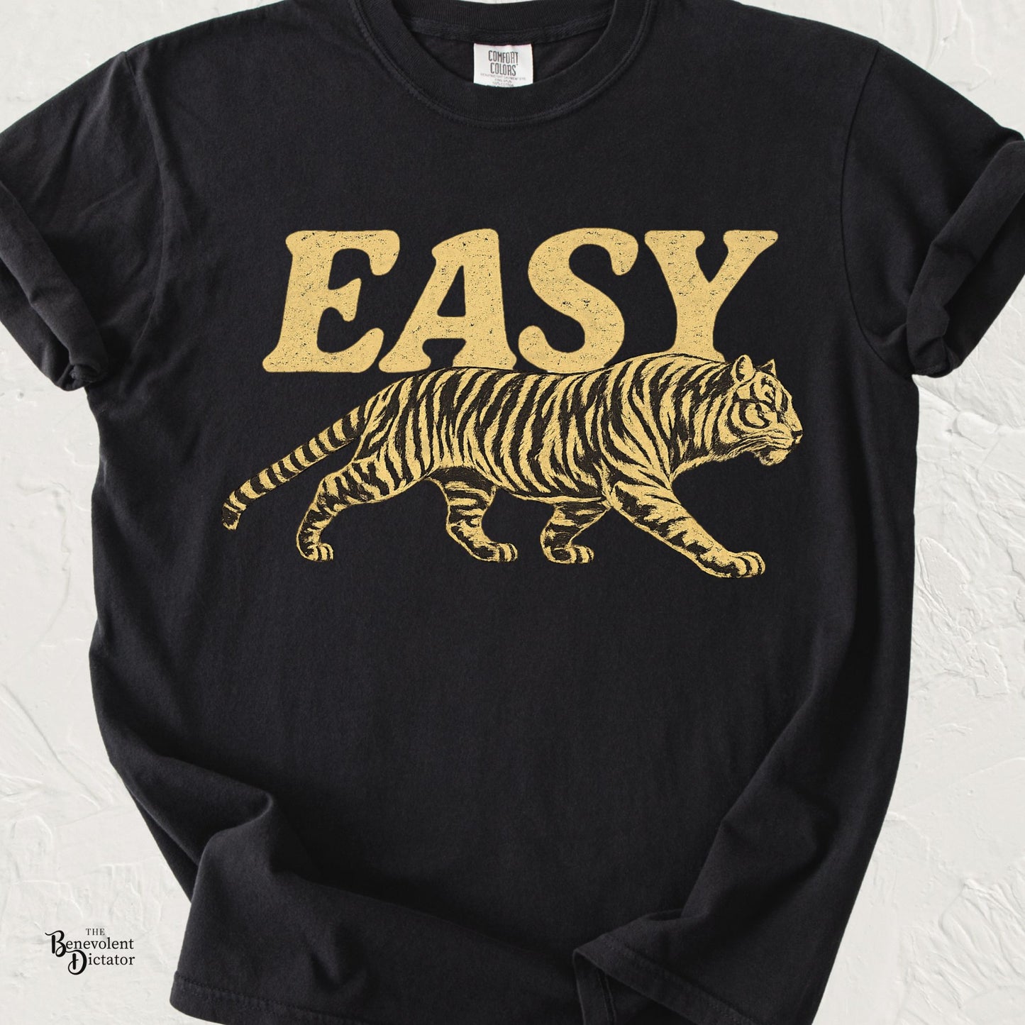 A black short-sleeve t-shirt with a distressed gold graphic of the word 'EASY' above a walking tiger, displayed on a light textured background.