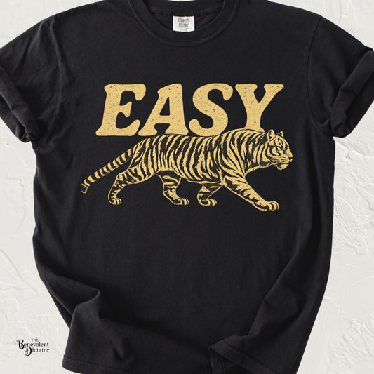 A black short-sleeve t-shirt with a distressed gold graphic of the word 'EASY' above a walking tiger, displayed on a light textured background.