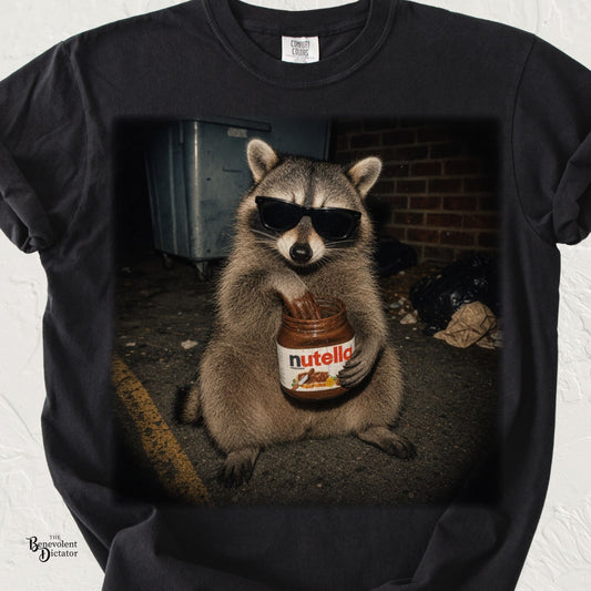 Funny raccoon graphic t-shirt featuring a raccoon wearing sunglasses and eating chocolate hazelnut spread from a jar in an alleyway.