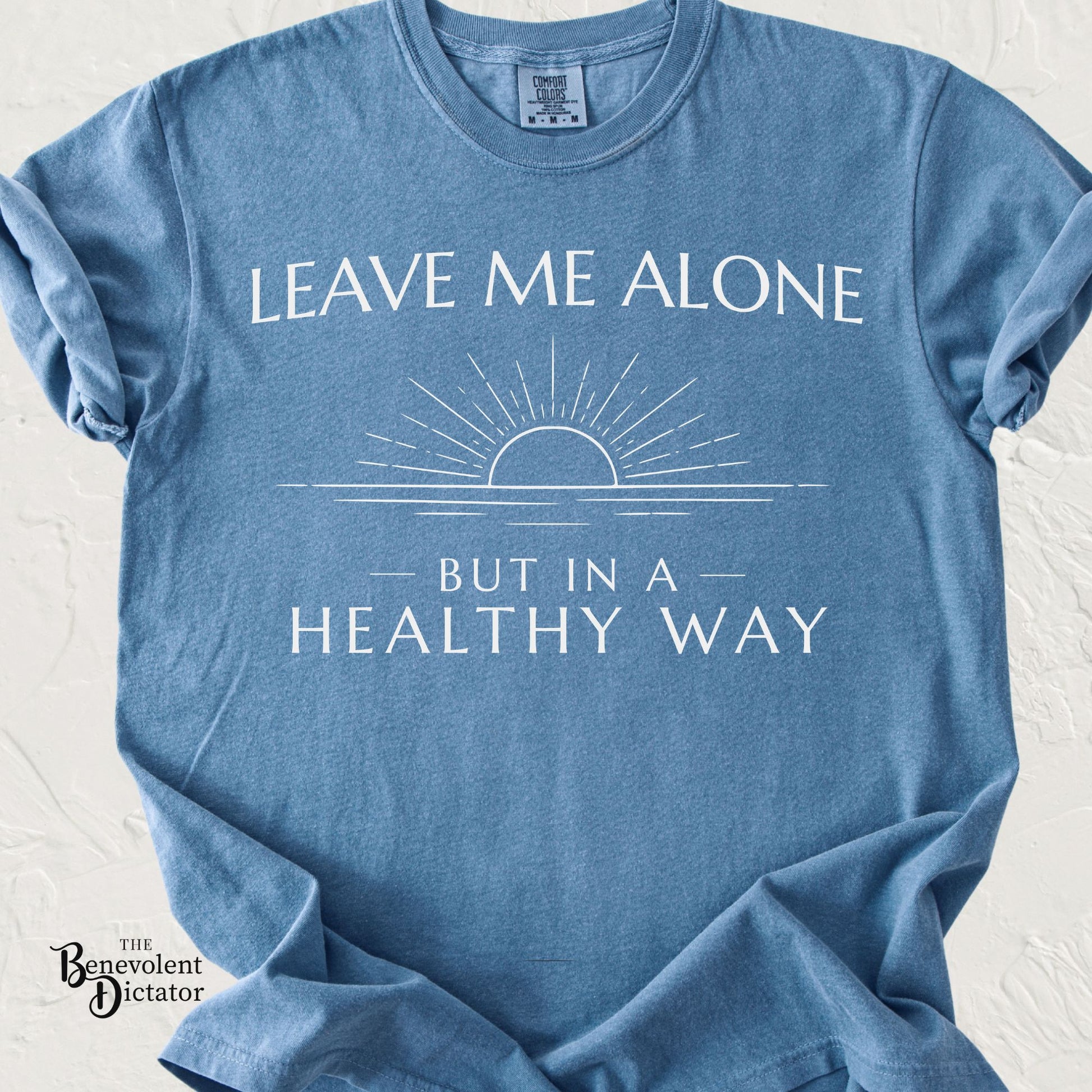 Minimalist t-shirt featuring the phrase Leave Me Alone But in a Healthy Way with a simple sunrise line art design.