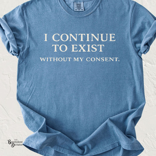 Minimalist typography T-shirt featuring the phrase "I Continue to Exist Without My Consent." printed in a vintage cream serif font on a blue Comfort Colors shirt.