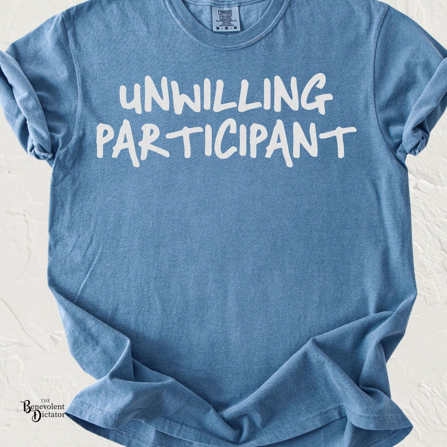 Minimalist typography t-shirt featuring the phrase "Unwilling Participant" in bold hand-drawn white lettering.