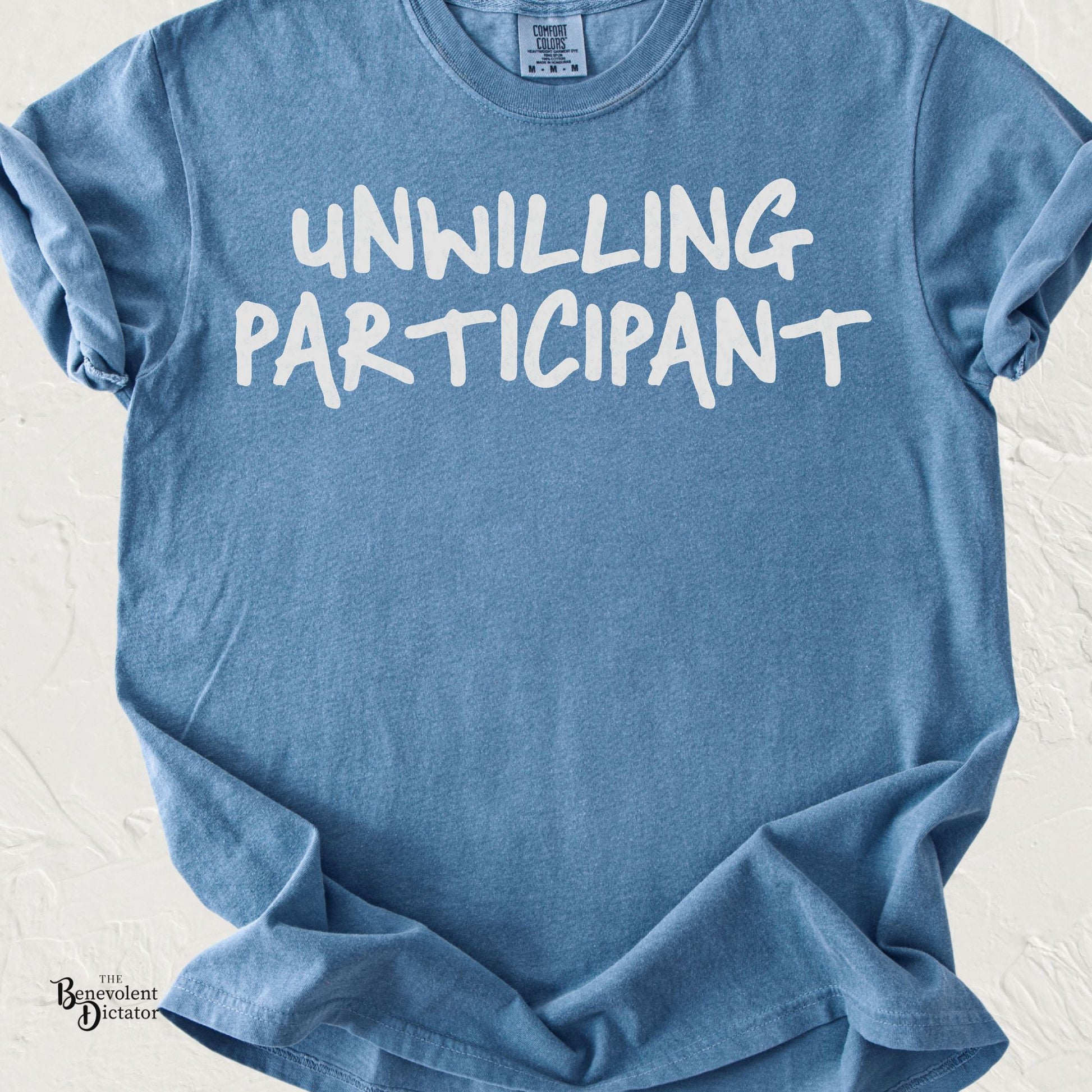 Minimalist typography t-shirt featuring the phrase "Unwilling Participant" in bold hand-drawn white lettering.