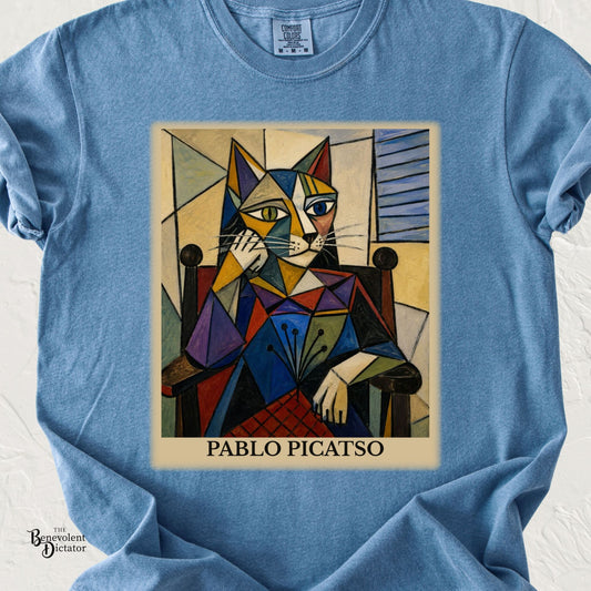 Blue Comfort Colors t-shirt featuring a colorful cubist-style cat portrait seated in a chair with the humorous artist-inspired name “Pablo Picatso.”