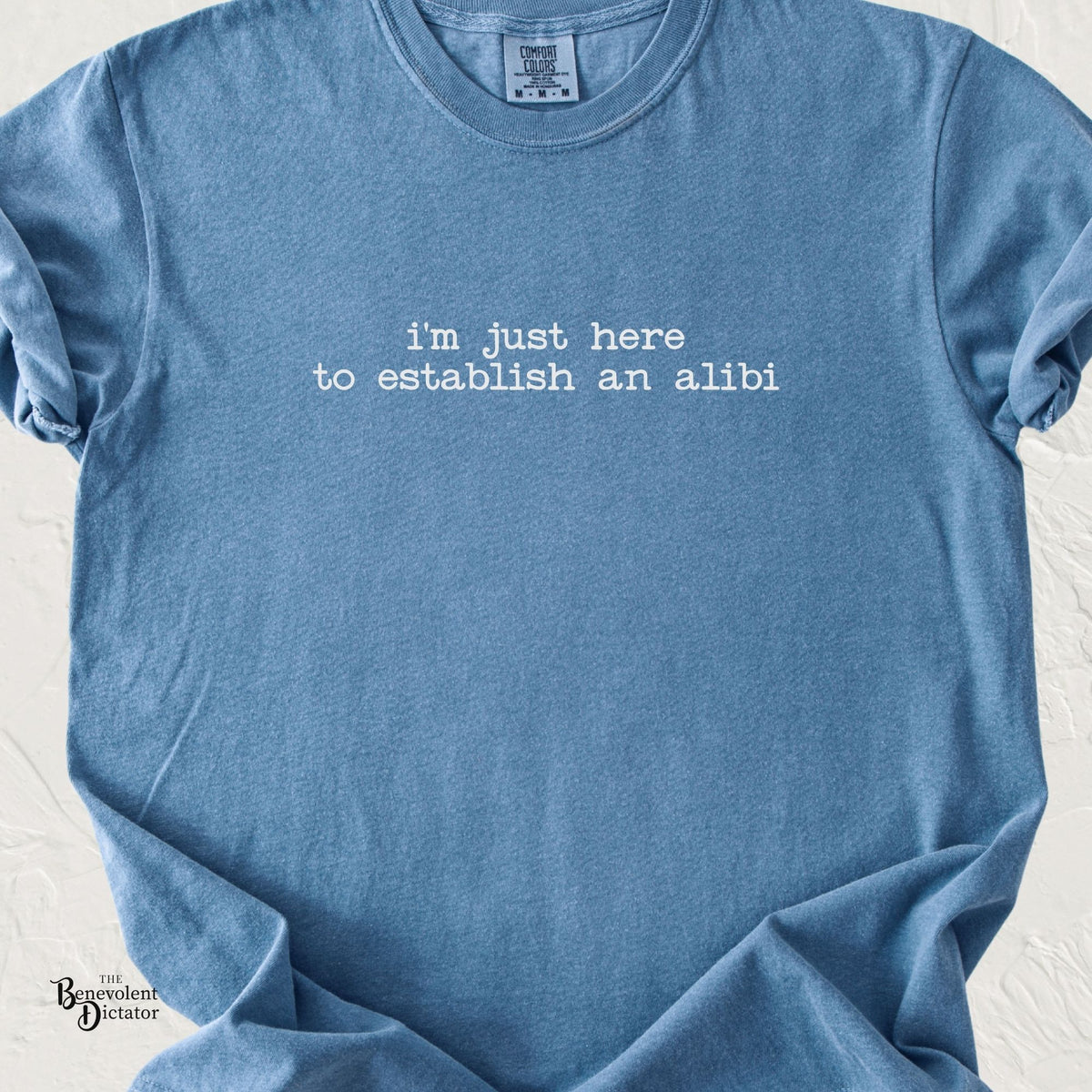 Blue Jean Comfort Colors t-shirt with minimalist typewriter text reading “I’m just here to establish an alibi” in light grey.