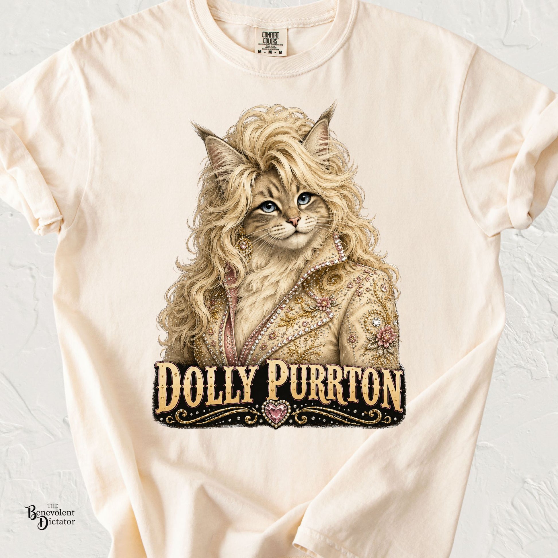 Long-haired cat styled with glamorous blonde curls and a rhinestone western jacket above the text "Dolly Purrton" on a Comfort Colors® t-shirt.