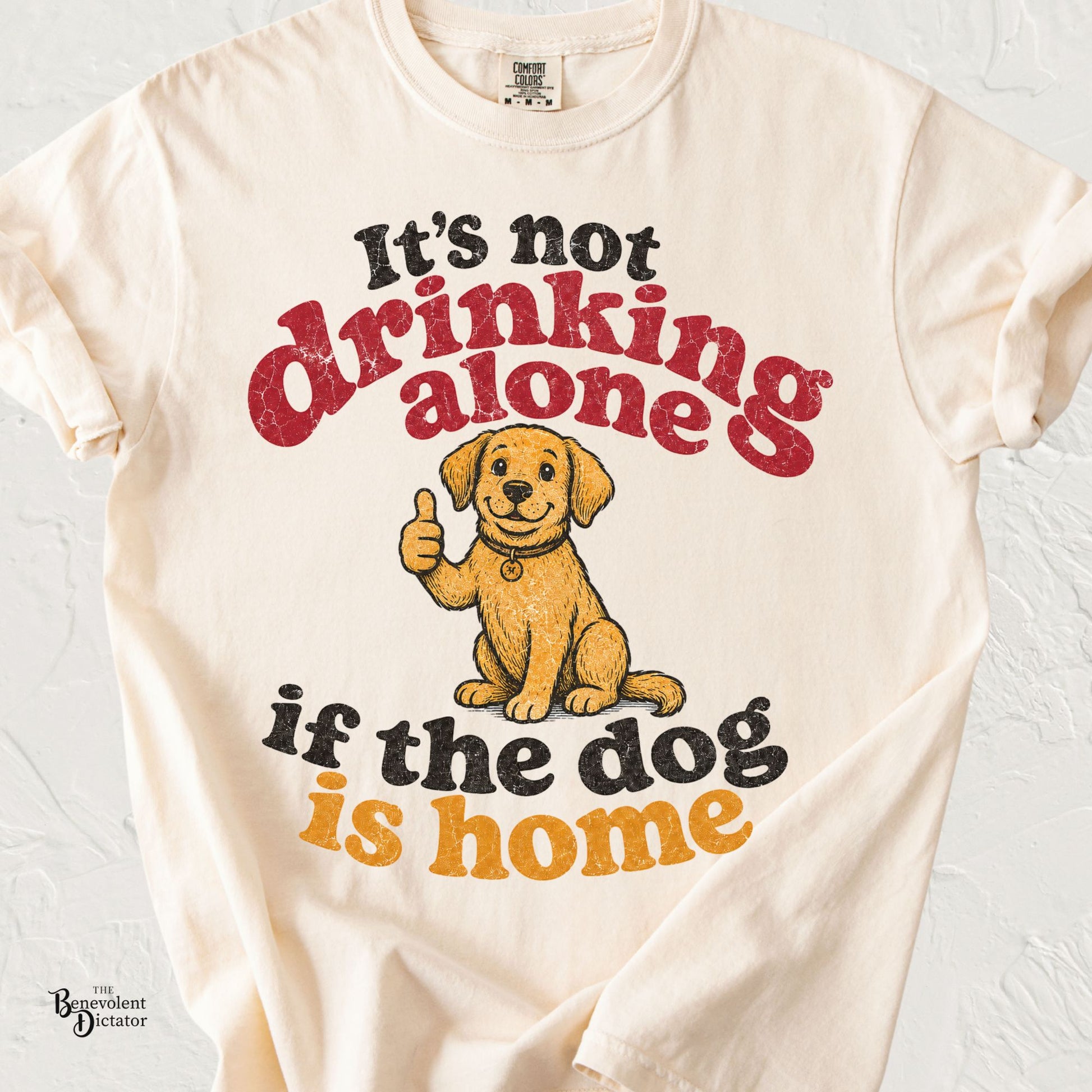 Retro typography shirt reading "It's Not Drinking Alone If the Dog Is Home" with a smiling dog giving a thumbs-up.