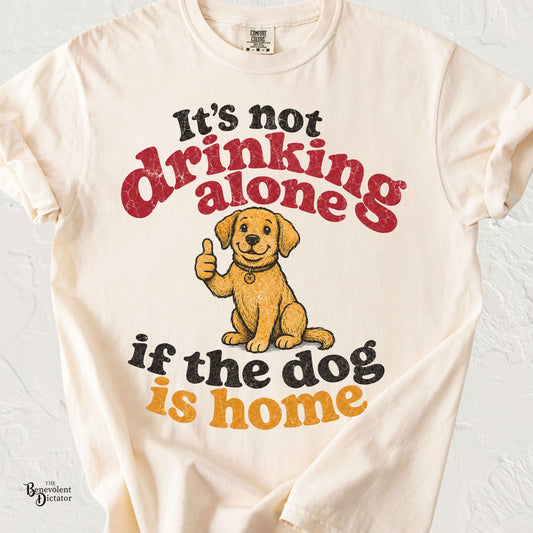 Retro typography shirt reading "It's Not Drinking Alone If the Dog Is Home" with a smiling dog giving a thumbs-up.