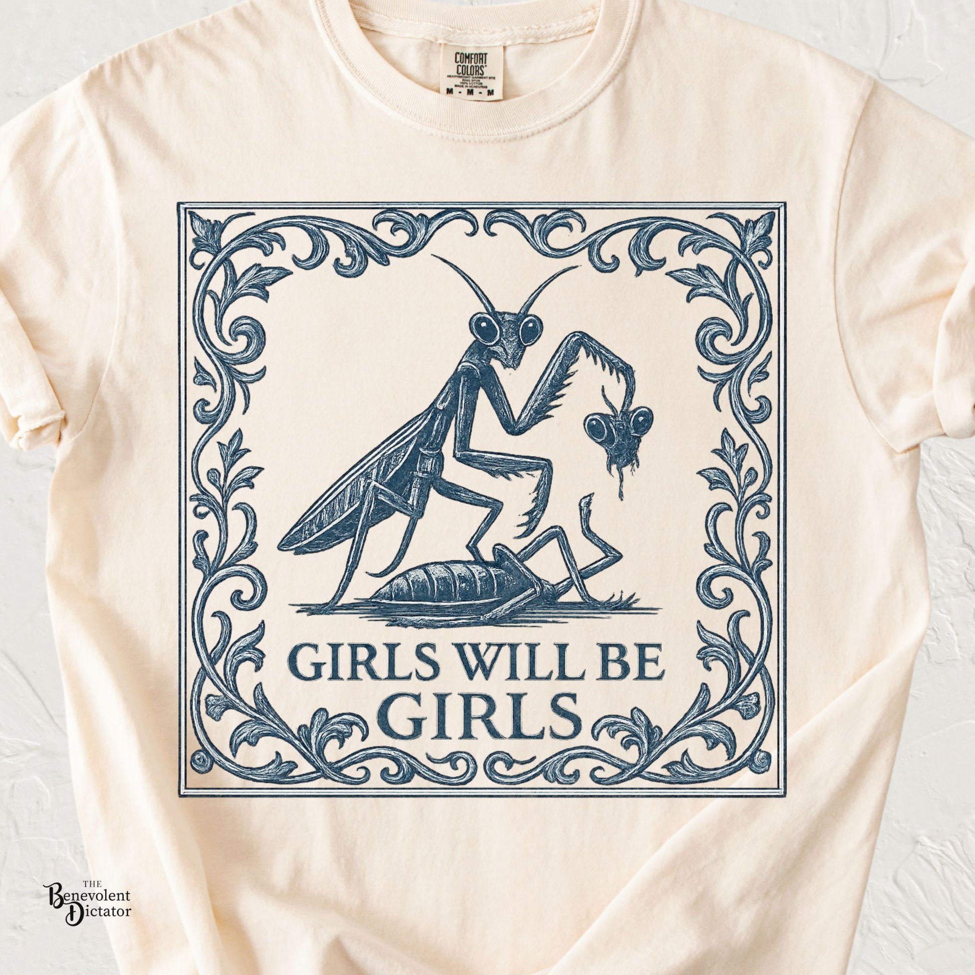 Vintage navy illustration of two praying mantises with ornate botanical framing and the phrase Girls Will Be Girls on an ivory Comfort Colors t-shirt.