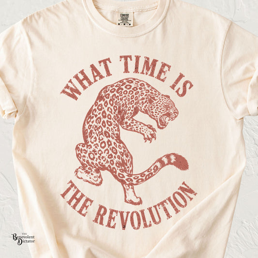 Ivory Comfort Colors t-shirt featuring a distressed rust-red leopard illustration with the phrase “What Time Is the Revolution” in curved vintage lettering.
