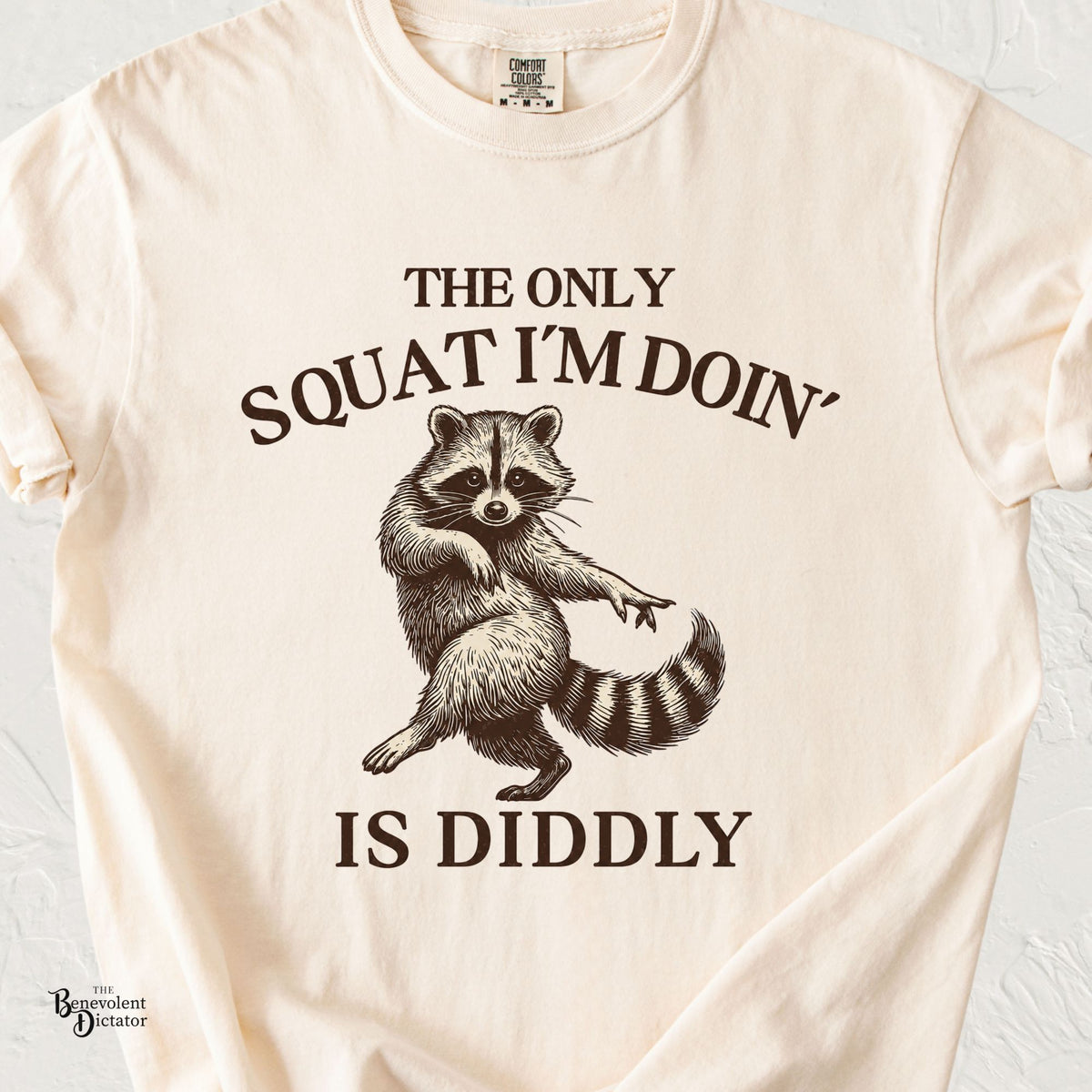 Funny raccoon squat graphic tee featuring vintage engraving artwork and The Only Squat I’m Doin’ Is Diddly typography
