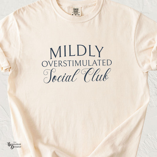 Ivory Comfort Colors t-shirt with navy typography reading Mildly Overstimulated Social Club in an elegant serif and script font combination.